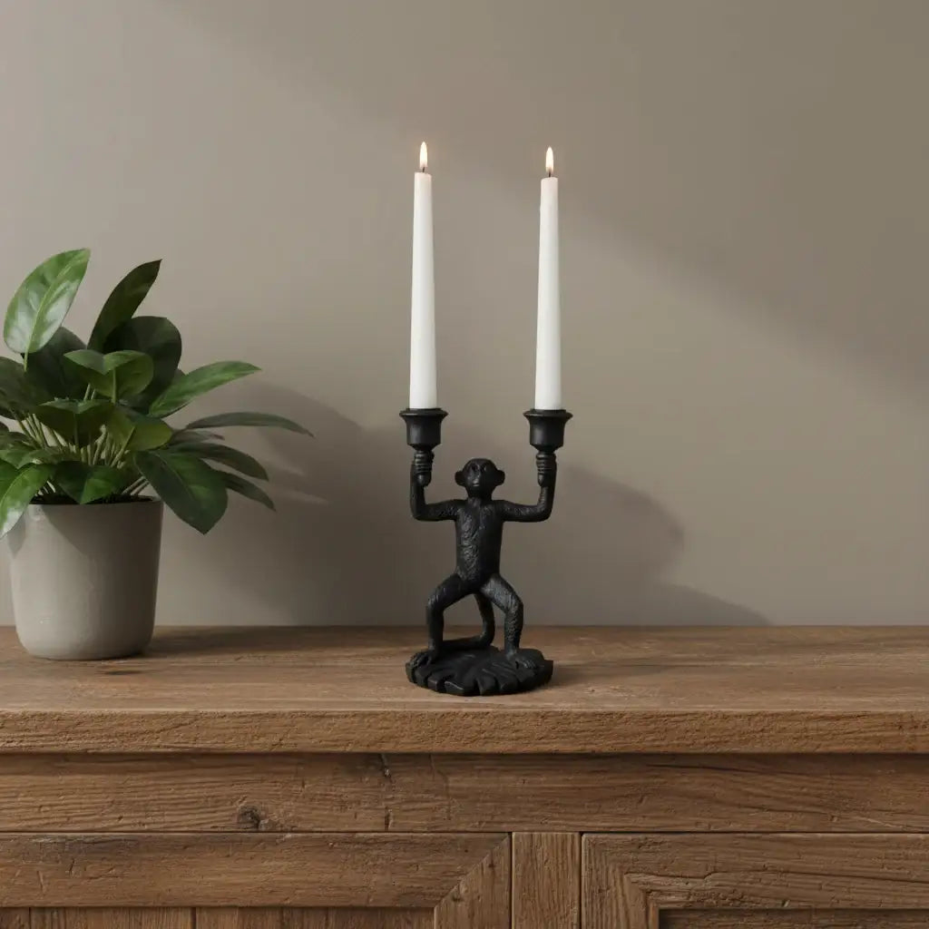 Black monkey-shaped candle holder with two lit white candles against a blue background