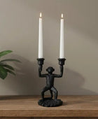 Black monkey-shaped candle holder with two lit white candles on a wooden surface.
