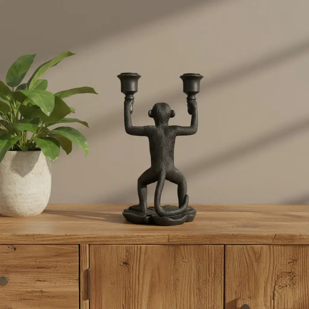 Decorative monkey candle holder on a wooden surface with a plant in the background