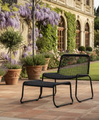 Black outdoor chair and ottoman on a patio with a garden and building in the background