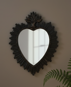 Heart-shaped mirror with decorative frame on a wall with a plant in the corner
