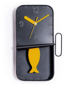 Black wall clock with yellow fish design and clock hands on a white background