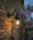 Black wall-mounted outdoor light fixture with clear glass shade on a light gray wall.