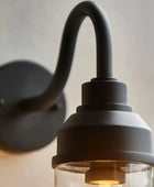 Black wall-mounted light fixture with clear glass shade on a neutral background