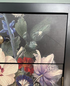 Close-up of a dark wood cabinet or drawer front featuring a floral print with blue, red, cream, and purple flowers on a dark background, with a round brass knob visible.