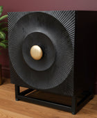 Decorative black speaker with gold center on a wooden floor against a maroon wall.
