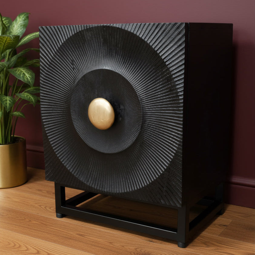 Decorative black speaker with gold center on a wooden floor against a maroon wall.