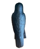 A black textured bird-shaped decorative object, shown from the back, standing on a light wood floor against a dark green wall.