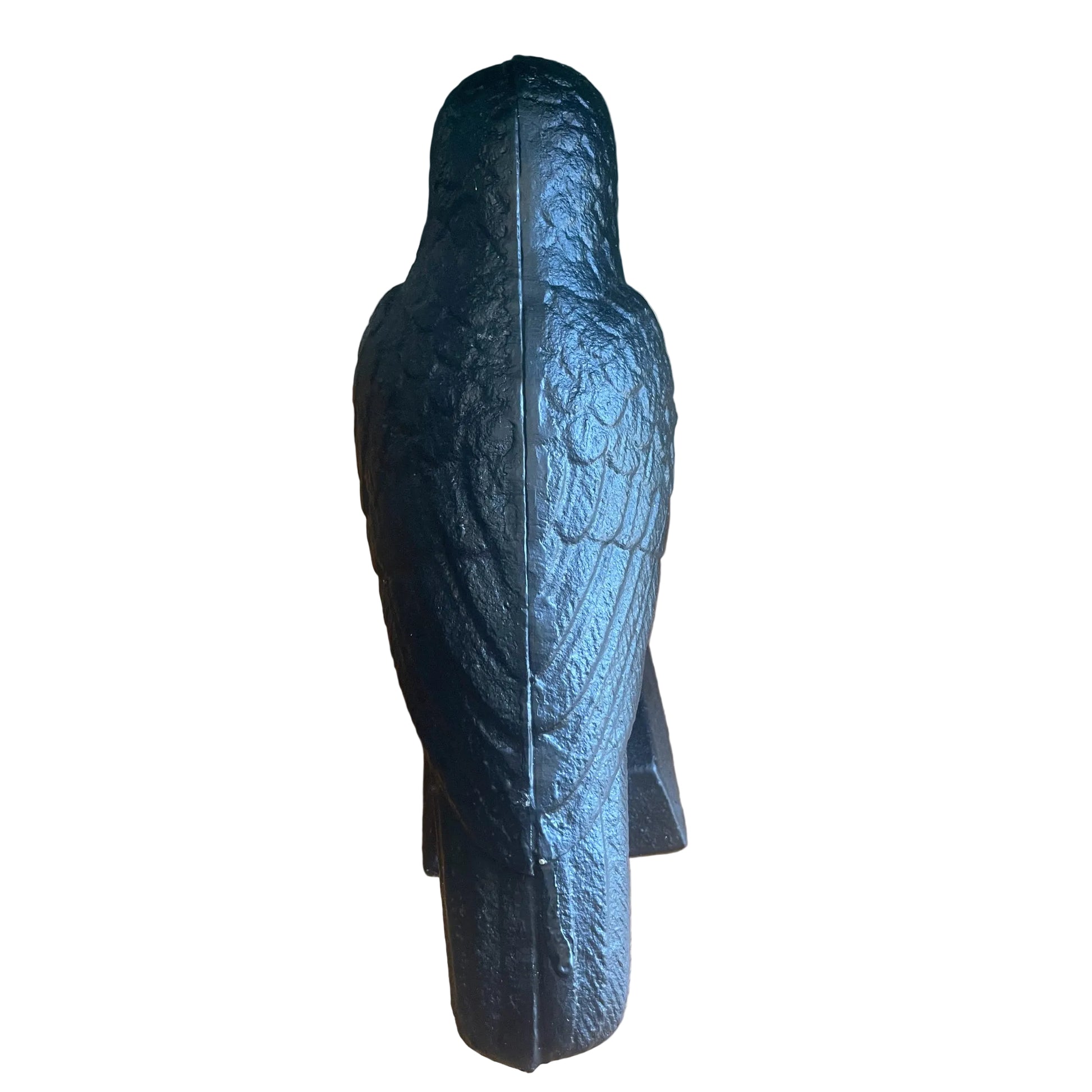 A black textured bird-shaped decorative object, shown from the back, standing on a light wood floor against a dark green wall.
