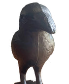 A dark cast-iron raven figurine standing on a wooden floor against a neutral wall.