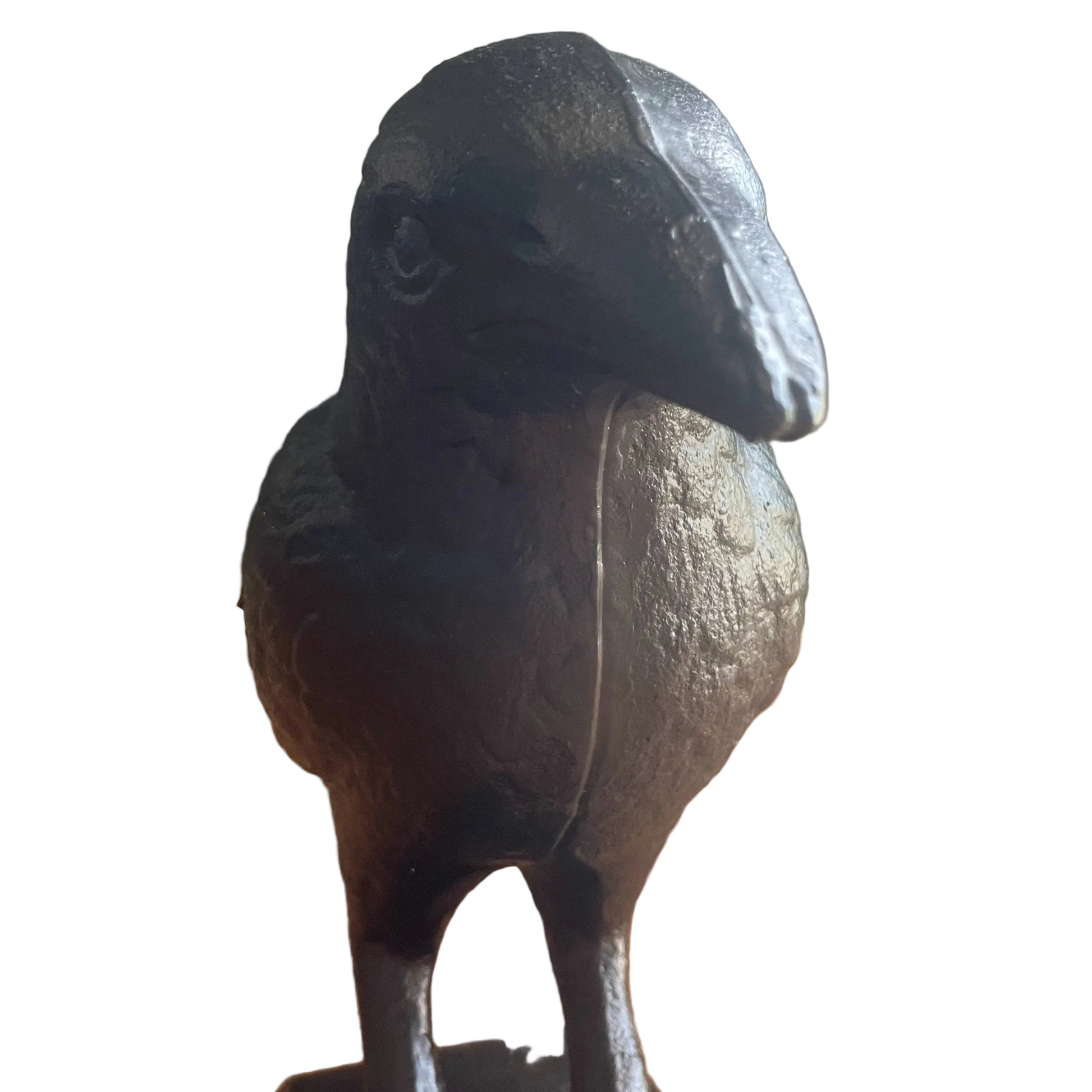 A dark cast-iron raven figurine standing on a wooden floor against a neutral wall.
