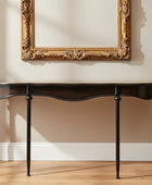 Dark wooden console table against a beige wall with an ornate gold frame.
