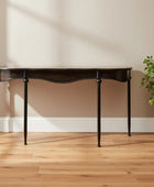 Dark wooden console table against a beige wall with a plant on a wooden floor.