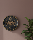 Wall clock with gear design on a brown wall with a plant to the right