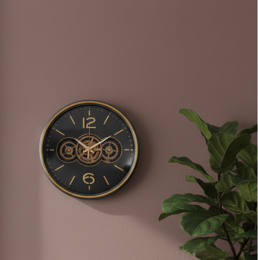 Wall clock with gear design on a brown wall with a plant to the right