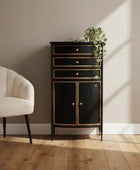 Black cabinet with gold accents next to a beige armchair on a wooden floor.