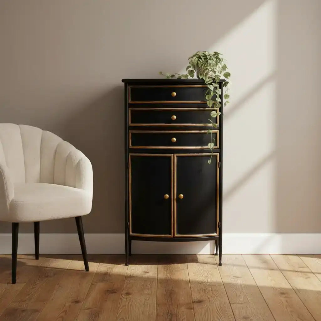 Black cabinet with gold accents next to a beige armchair on a wooden floor.