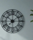 Decorative wall clock with black metal frame and Roman numerals on a light gray wall.