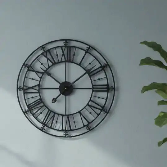 Decorative wall clock with black metal frame and Roman numerals on a light gray wall.