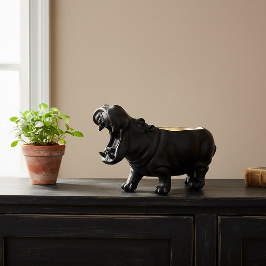 Black hippo figurine on a wooden surface next to a potted plant