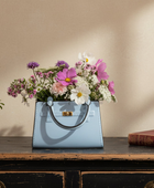 Blue handbag filled with flowers on a wooden surface with a beige wall background