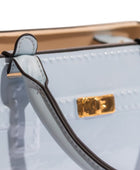 Close-up of a light blue handbag with a gold logo tag on a white background