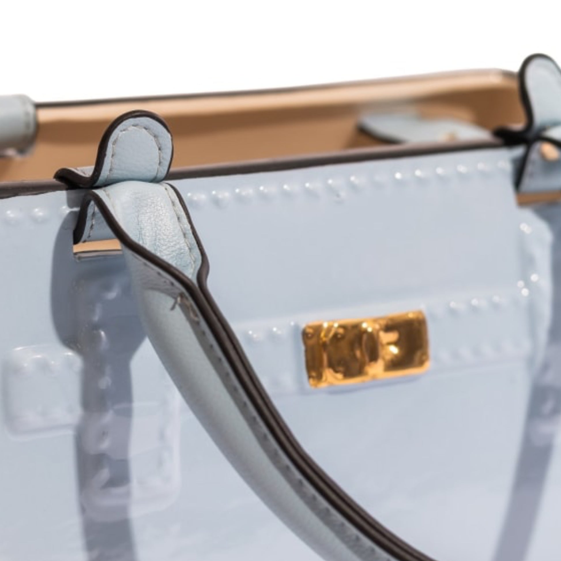 Close-up of a light blue handbag with a gold logo tag on a white background