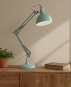 Teal desk lamp on a wooden surface with a plant and book in the background