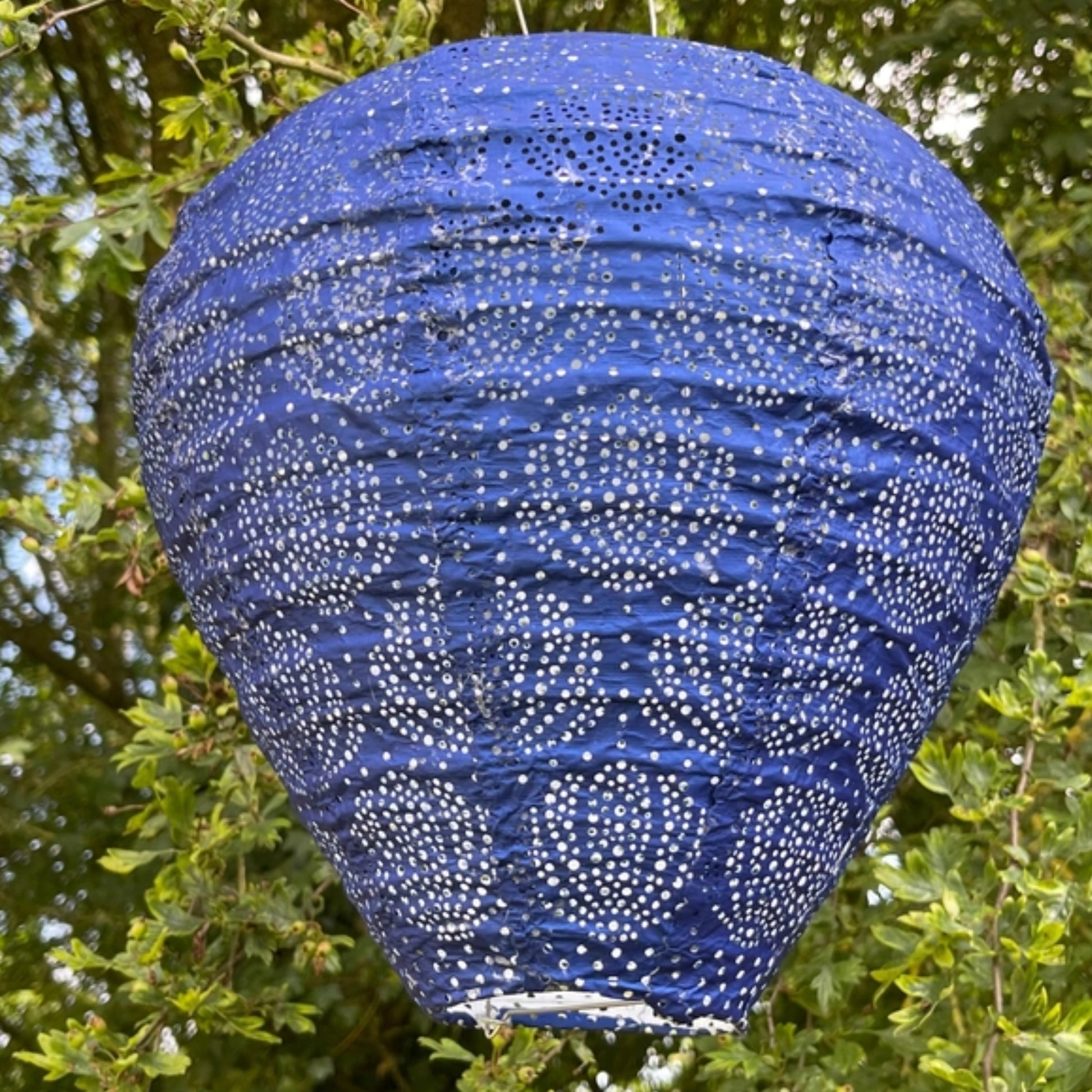Blue paper lantern with white patterns hanging among green leaves