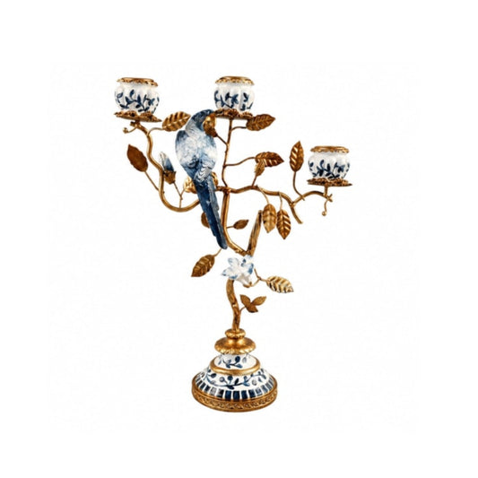 An ornate three-light candelabra designed as a bird perched on a flowering branch, featuring a gold-finished metal frame with blue and white porcelain-style details on the bird, flowers, and base, set against a plain white background.