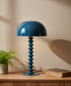 Blue table lamp on a wooden surface with a plant and book in the background