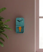 Blue wall clock with fish design on a brown wall next to a plant