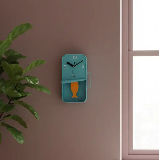 Blue wall clock with fish design on a brown wall next to a plant