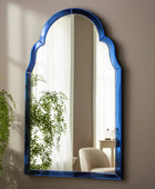 Blue-framed mirror on a wall with a plant in the foreground