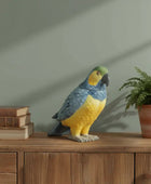 Decorative parrot sculpture on a wooden surface with books and a plant.