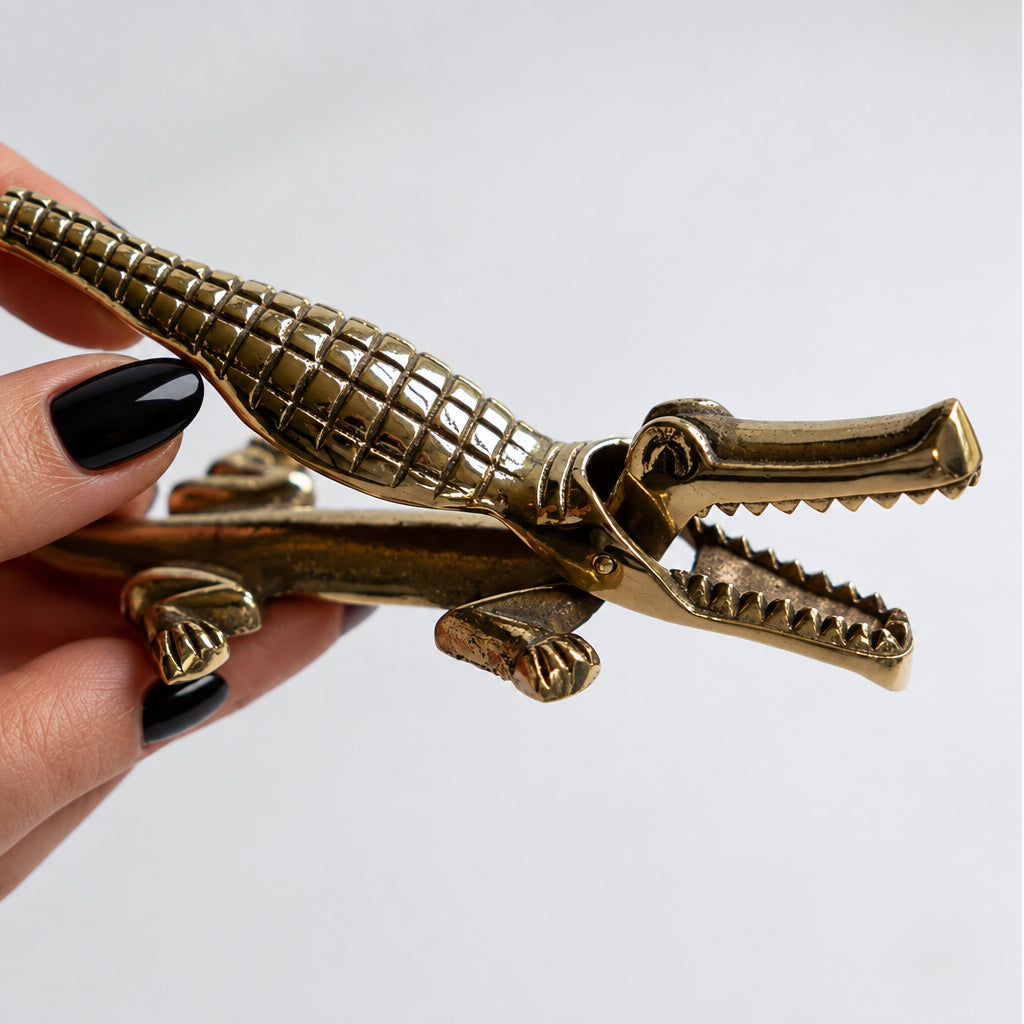 A brass crocodile-shaped door stopper held by a hand against a plain light gray background.