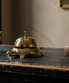 Gold turtle-shaped bell on a wooden surface with a plant and book in the background