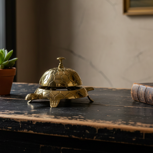 Gold turtle-shaped bell on a wooden surface with a plant and book in the background