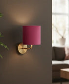Wall-mounted lamp with pink shade on a gray wall next to a living room setting.