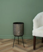 Decorative metal vase on a wooden floor against a green wall with a white chair.