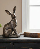 Bronze rabbit sculpture on a wooden surface with a plant and book in the background.