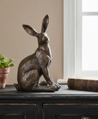 Bronze rabbit sculpture on a wooden surface with a plant and book in the background