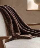 Brown knitted blanket draped over a light-colored sofa in a cozy room.