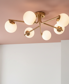 Modern ceiling light fixture with six spherical glass shades on a pink and white wall background