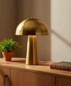 Gold table lamp on a wooden surface with a plant and book in a warm setting