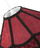 Close-up of a red patterned fabric lampshade with black braided trim and a white hanging cord visible at the top, photographed against a white background.
