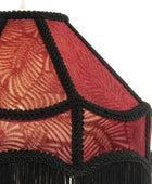 Close-up of a decorative lampshade with a red and gold leaf patterned fabric and black braided trim with fringe at the bottom, set against a plain white background.