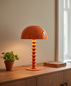 Orange table lamp on a wooden surface with a plant and book in the background