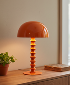 Orange table lamp on a wooden surface with a plant and book in the background