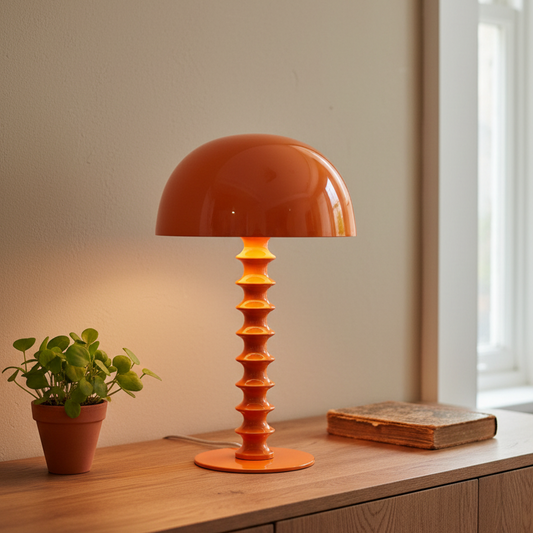 Orange table lamp on a wooden surface with a plant and book in the background